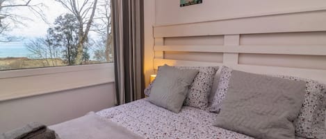A bedroom with a bed, a window with curtains, a lamp, and a painting on the wall.