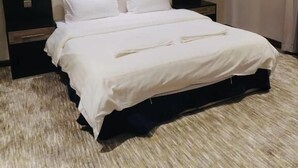 A modern hotel room with a large bed, a headboard with built-in lighting, a bedside table, and a door with a handle. - Ziyara for Serviced Apartments (Riyadh)