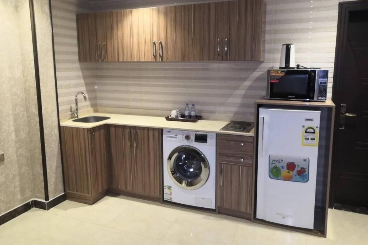 A compact kitchen with wooden cabinets, a washing machine, a refrigerator, and a microwave.