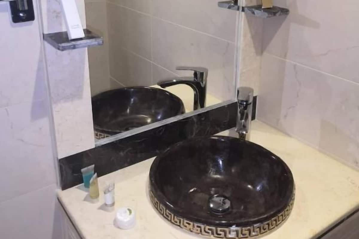 A bathroom with a large mirror, a black sink with a decorative pattern, and a shower area.