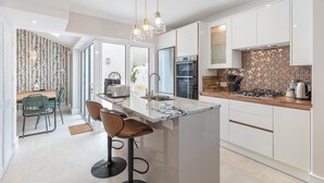 Una cocina moderna con armarios blancos, una isla de mármol y un salpicadero de azulejos pequeños.