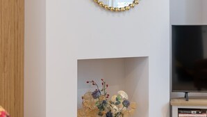 Una sala de estar con un espejo, una chimenea, un televisor y un jarrón amarillo con flores.
