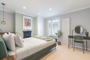 A bedroom with a bed, a desk, a chair, a radiator, a window with shutters, and a hanging light fixture. - Stylish 3-bed townhouse in central Brighton, moments from the North Laine and station. Recently renovated to a high standard with open-plan living, private patio, and space for up to 6 guests. (Brighton)