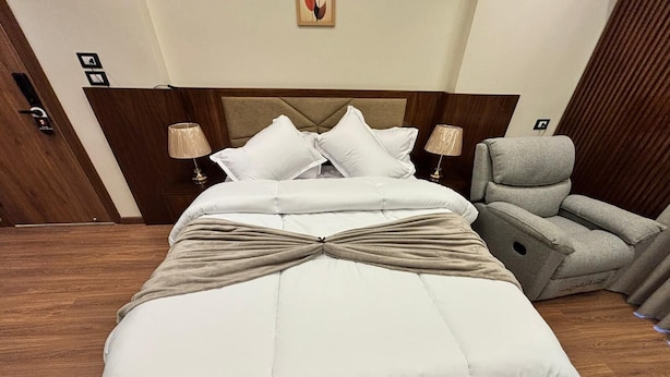 A large bed with a tufted headboard, two bedside lamps, and a gray reclining chair. - Sheraton Star (Alexandria)