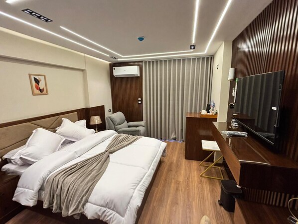 A hotel room with a bed, a desk, a television, an air conditioning unit, and a curtain.