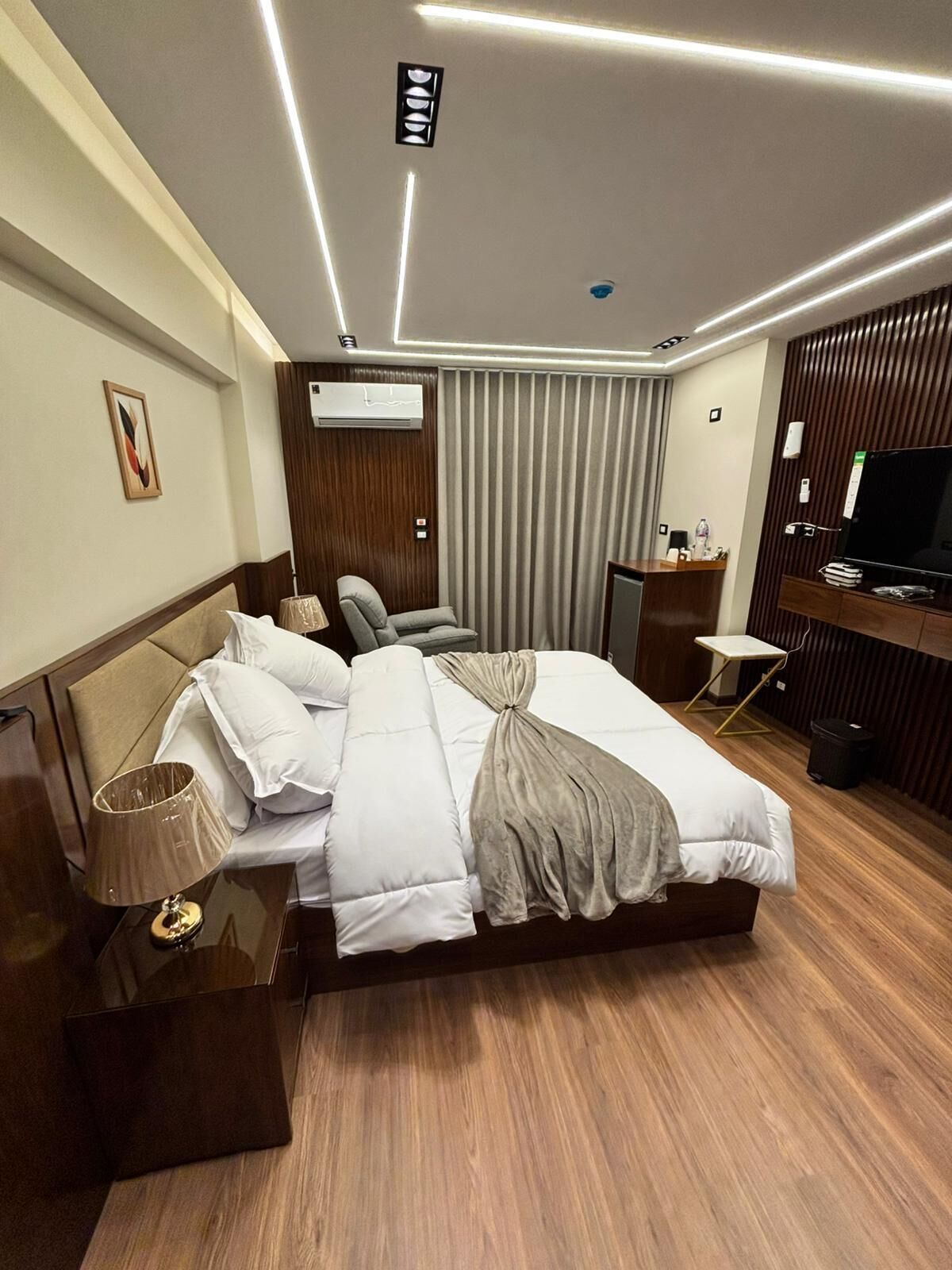 Una habitación de hotel moderna con cama, mesita de noche, lámpara y televisor.