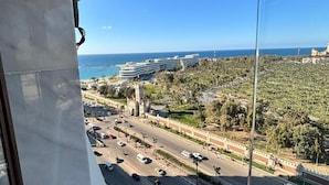 A view from a balcony overlooking a coastal cityscape with a road, buildings, and a clear sky. - Sheraton Star (Alexandria)