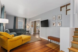 Ein Wohnzimmer mit einer Couch, einer Bank, einem Fernseher und einer Treppe.