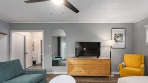 Ein modernes Wohnzimmer mit einer Couch, einem Fernseher, einem gelben Sessel und einem gemusterten Teppich.