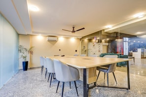 Una sala de reuniones moderna con una mesa larga, sillas, un ventilador de techo y un panel de vidrio.