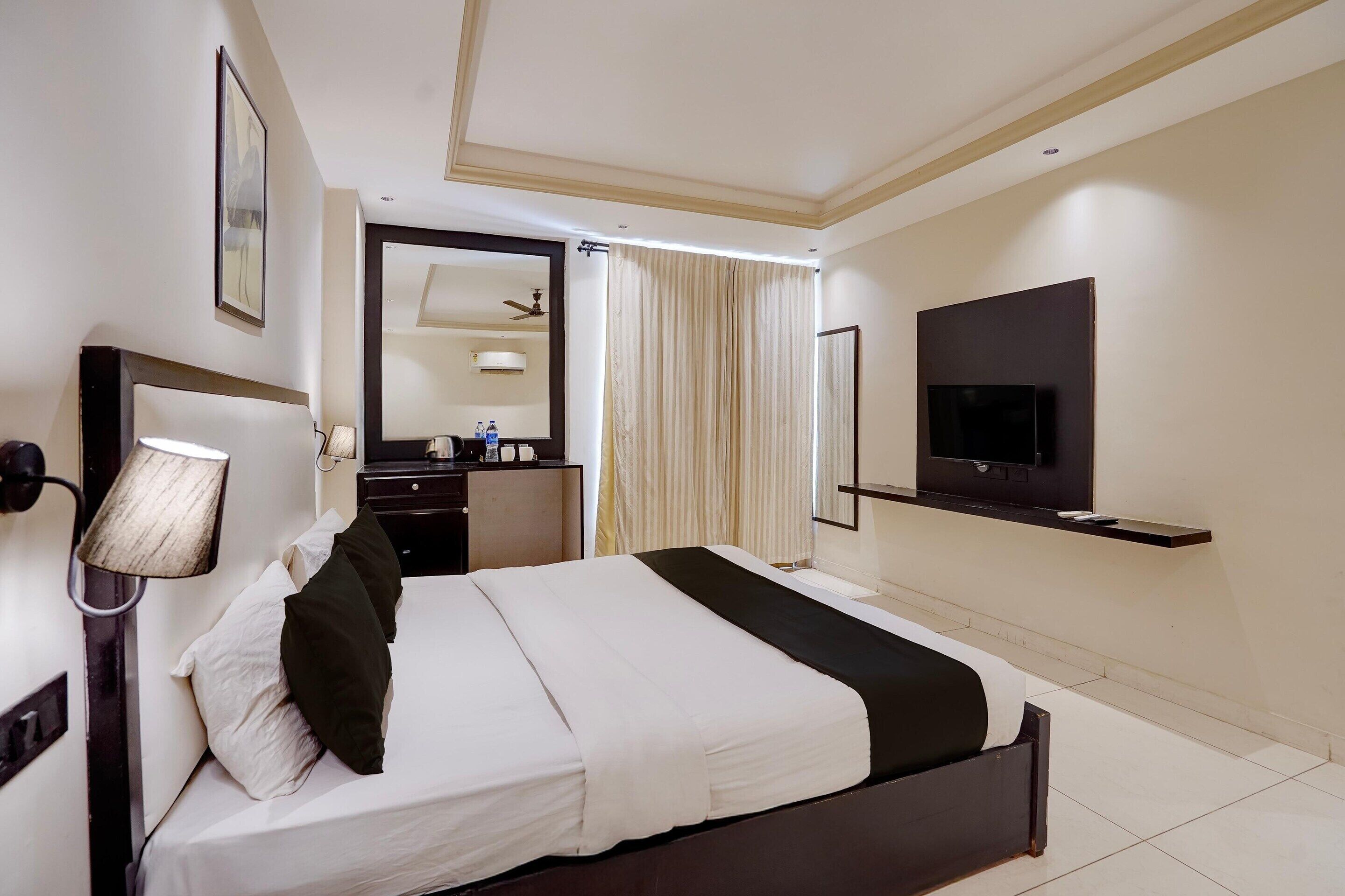 Una habitación de hotel con cama, escritorio, silla, televisor y espejo.