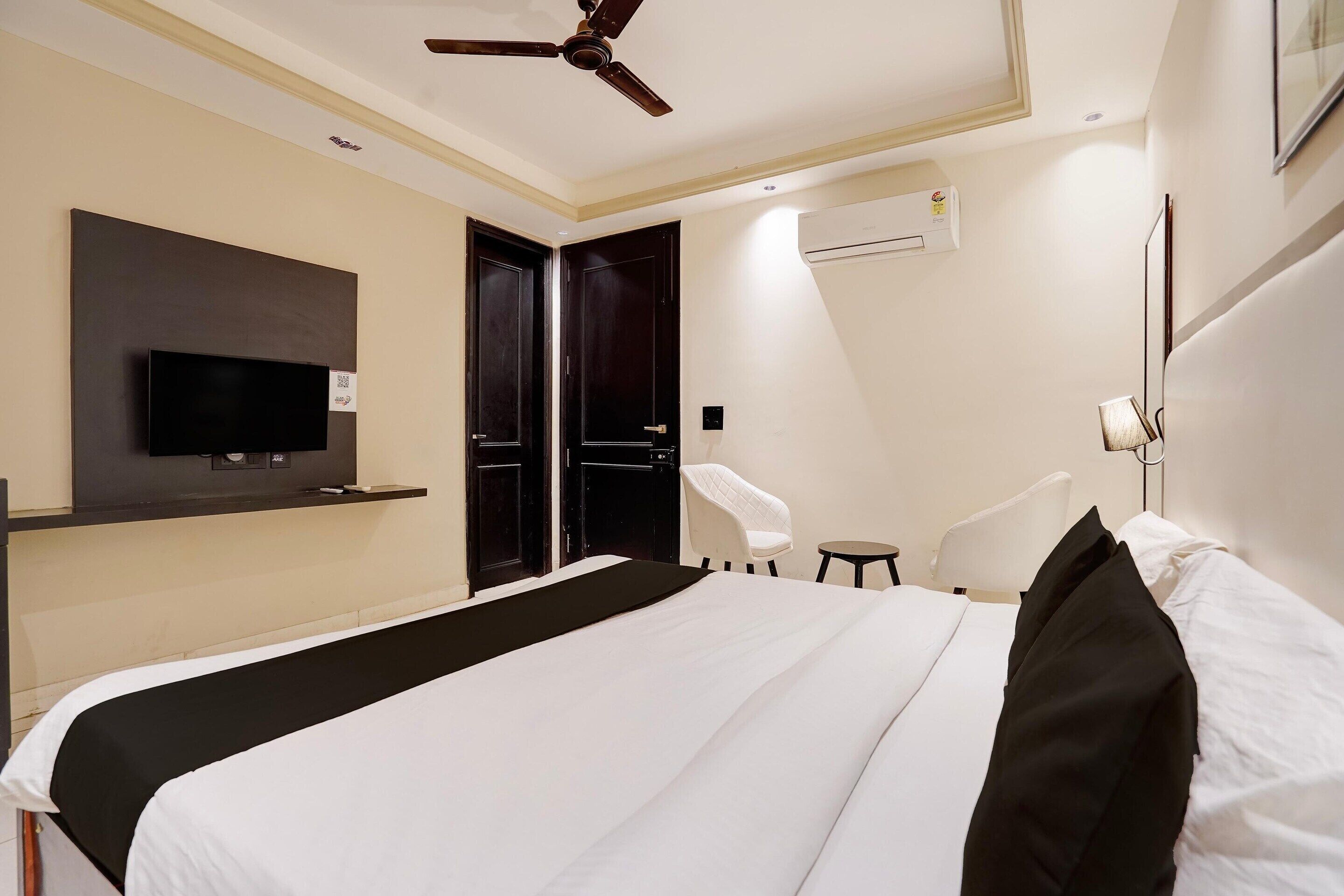 Habitación de hotel con cama, televisión montada en la pared, ventilador de techo y aire acondicionado.