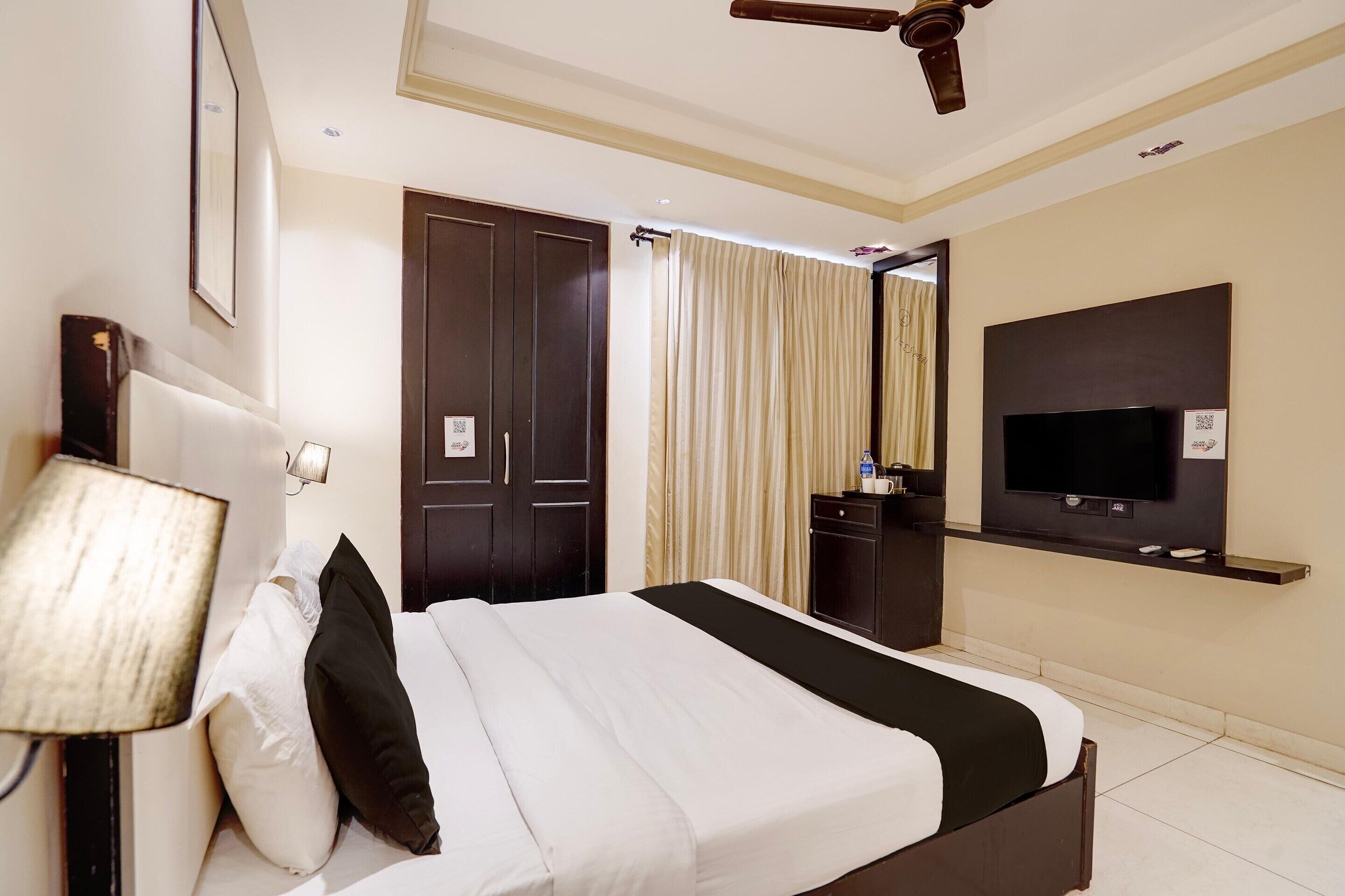 Una habitación de hotel con cama, televisión, escritorio, lámpara y ventilador de techo.