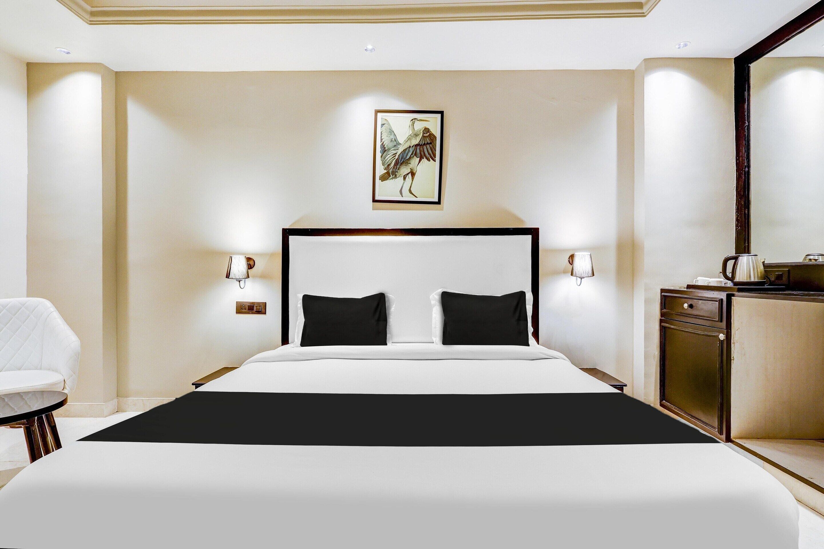 A hotel room with a large bed, a bedside table, a chair, and a painting on the wall.