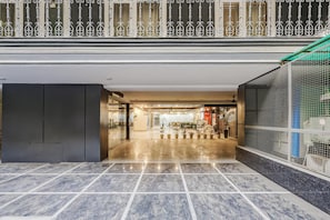 Un hall espacioso con piso de mármol, barandilla metálica y puerta de vidrio que da a un restaurante.