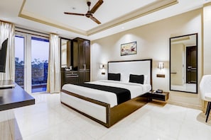 Un dormitorio con cama, escritorio, silla, ventilador de techo, un espejo grande y un cuadro en la pared.