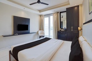 A hotel room with a bed, a television mounted on the wall, a chair, a desk with a water bottle, and a wardrobe. - Deluxecloud Bay (Gurugram)