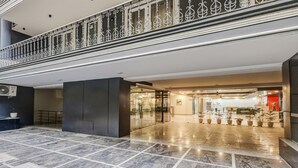 Een moderne hotelentree met een marmeren vloer, een receptiebalie en een glazen deuropening.