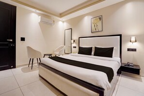 Een moderne slaapkamer met een groot bed, een stoel, een nachtkastje, een spiegel en een schilderij aan de muur.