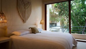 A bedroom with a large bed, two bedside lamps, a macrame wall hanging, and a balcony with a view of greenery. - 3BR Jungle Escape with luxe plunge Pool- Holistika (Tulum)