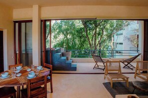 A dining area with a table set for four, a balcony with a view of trees, and a staircase leading to an upper level. - 3BR Jungle Escape with luxe plunge Pool- Holistika (Tulum)