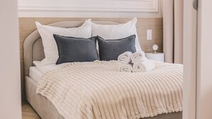 A neatly made bed with a textured blanket and rolled towels, a wooden headboard, and a bedside table with a small clock. - Estilo Designerski Apartament z Tarasem (gmina Parzęczew)