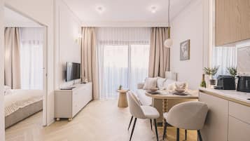 Una habitación de hotel moderna con una cama, un televisor, una zona de comedor con mesa y sillas, y una kitchenette.
