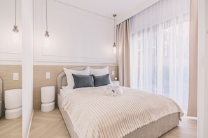 A modern hotel room with a large bed, a bedside table, a lamp, and a window with sheer curtains. - Estilo Designerski Apartament z Tarasem (gmina Parzęczew)