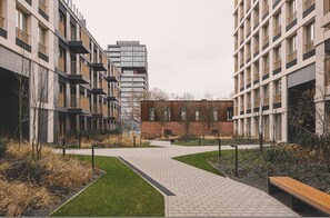 A modern building complex with a central pathway, surrounded by greenery and benches.