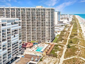 Un hotel moderno de gran altura con múltiples balcones, piscina en la azotea y vista al mar.