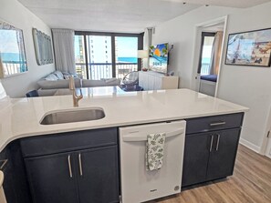Een moderne keuken met een groot eiland, een ingebouwde vaatwasser en donkere kastjes.