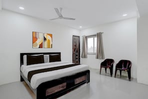 Ein Schlafzimmer mit Bett, Deckenventilator, Kunstwerken, Fenster mit Vorhängen und zwei Stühlen.