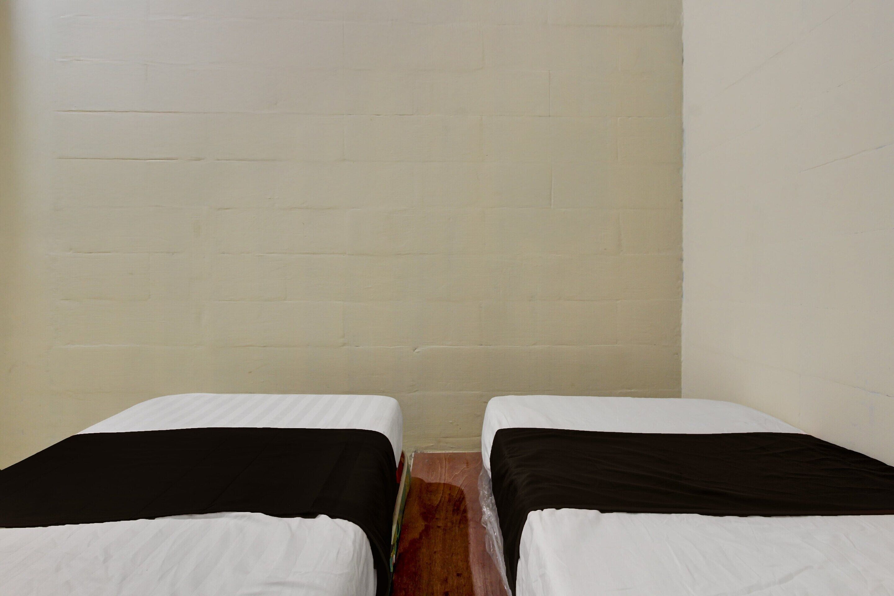 Dos camas individuales con ropa de cama blanca y negra, piso de madera y una pared de ladrillo blanco sin adornos.