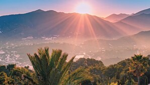 A mountain landscape with a sunrise or sunset, palm trees, and a valley with buildings. - Villa Verdejo Luxury 2-Bedroom, 2-Bathroom Apartment with Pool & Spa (Olivella)