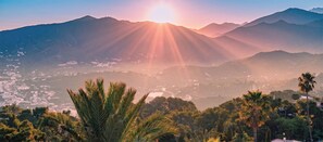 A mountain landscape with a sunrise or sunset, palm trees, and a valley with buildings. - Villa Verdejo Luxury 2-Bedroom, 2-Bathroom Apartment with Pool & Spa (Olivella)