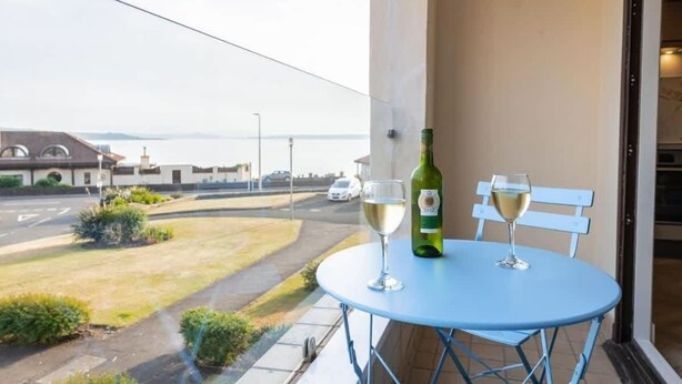 A balcony with a table, two chairs, a bottle of wine, and two glasses. - Hame By The Sea, Super Apartment (Largs)