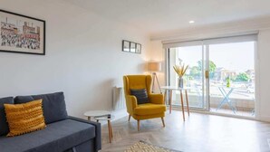 A modern living room with a sofa, a yellow armchair, a small table, and a large window with a view of the street. - Hame By The Sea, Super Apartment (Largs)