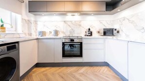 A compact kitchen with white cabinets, a built-in oven, a microwave, and a washing machine. - Hame By The Sea, Super Apartment (Largs)