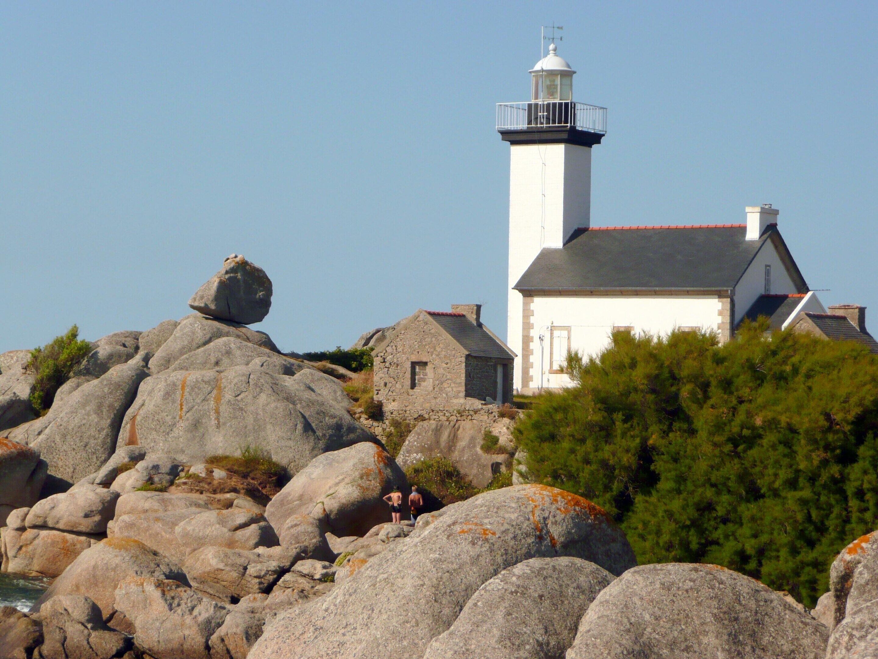 A lighthouse with a white tower and black top, surrounded by large rocks and trees.