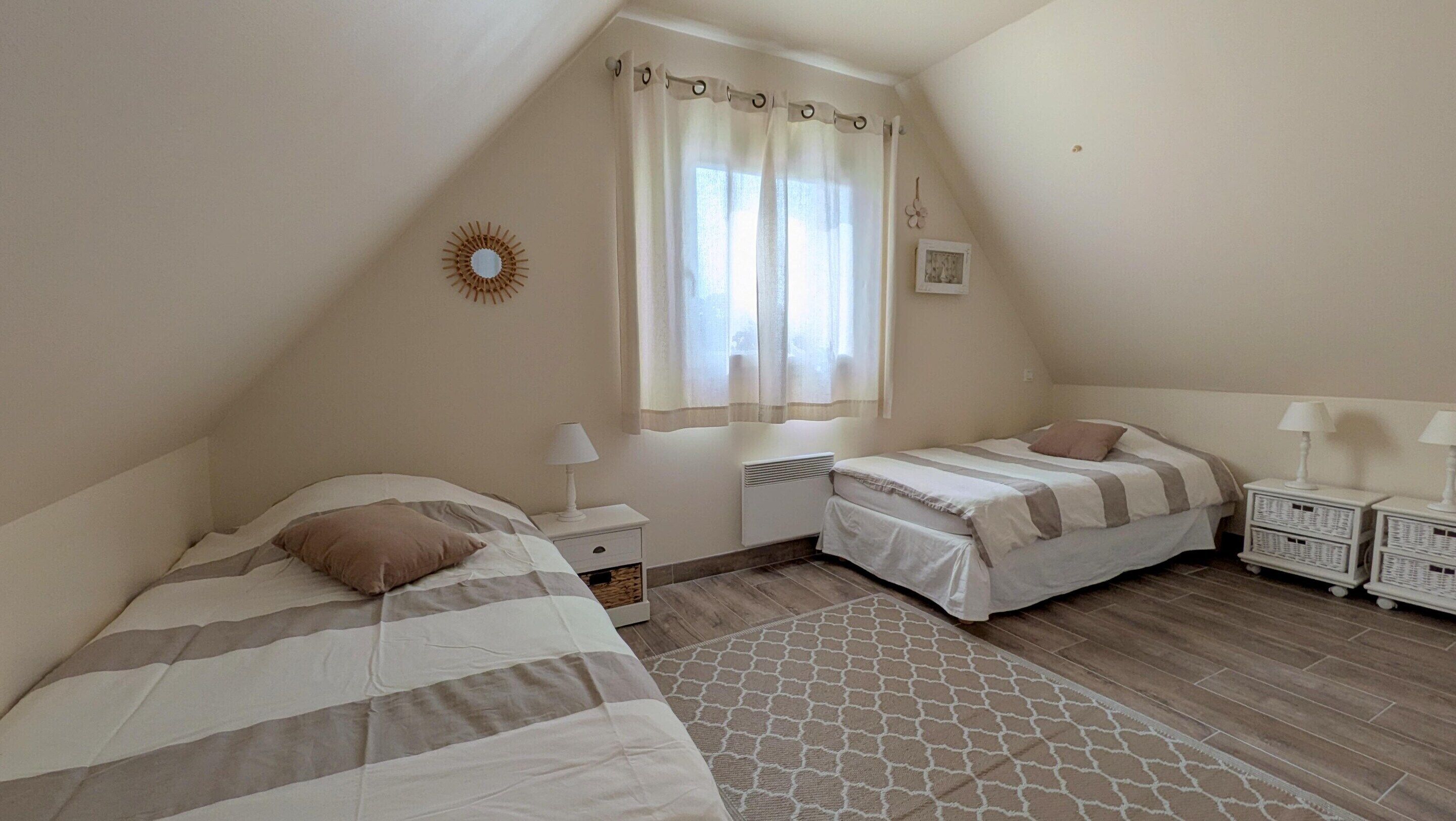 A bedroom with two beds, a window with curtains, a radiator, and a patterned rug.
