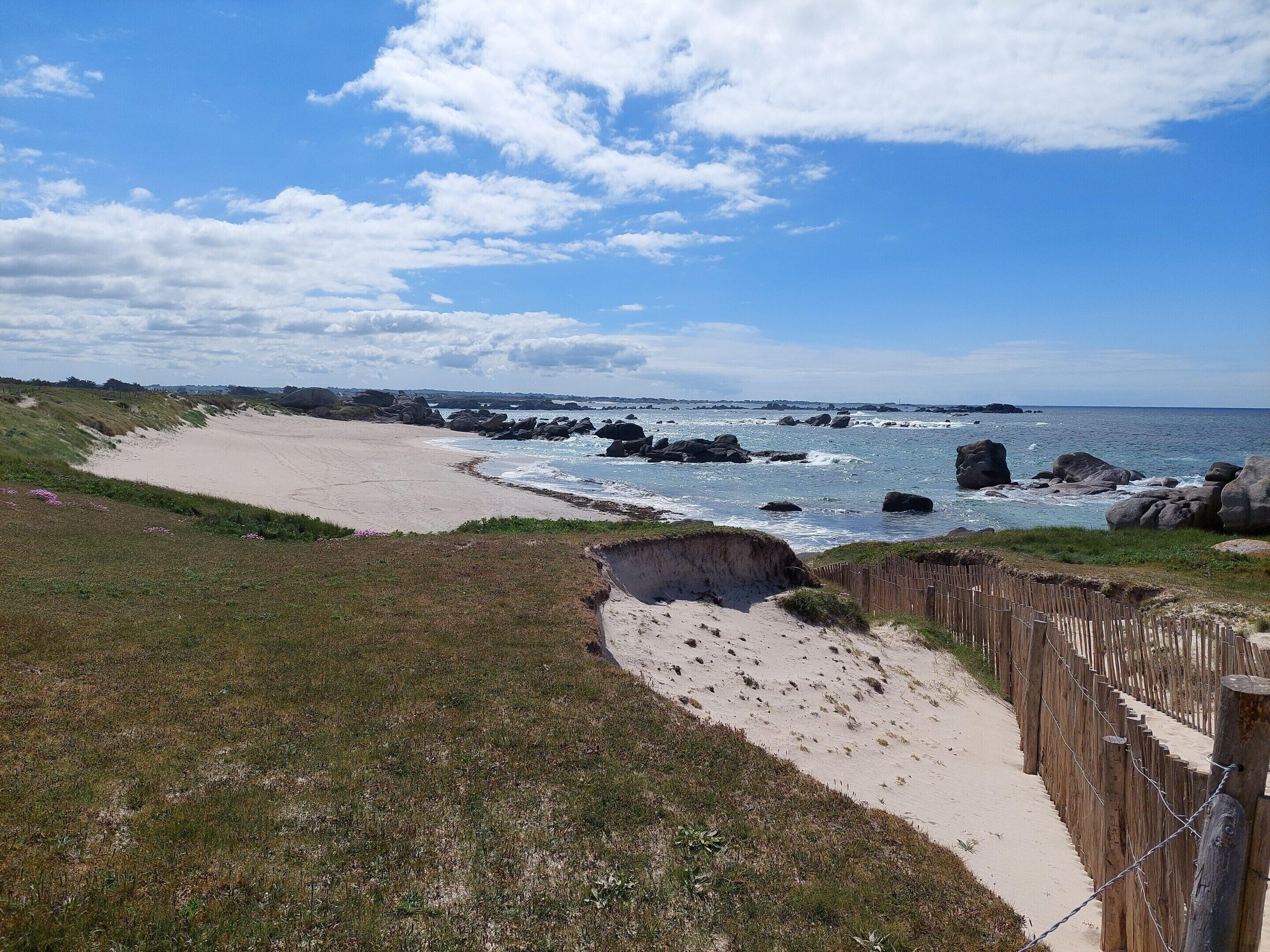 A coastal landscape with a sandy beach, rocky outcrops, and a wooden fence.