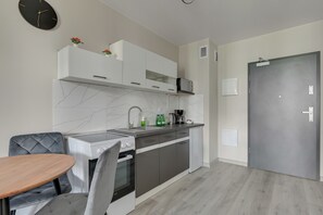 A modern kitchen with a stove, oven, sink, and white cabinets. There is a dining table with chairs and a clock on the wall. - Mostek 246 - Grey by Grand Apartments (Gdańsk)