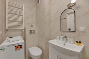 A bathroom with a white toilet, a sink with toiletries, a towel on the dryer, and a mirror. - Mostek 246 - Grey by Grand Apartments (Gdańsk)