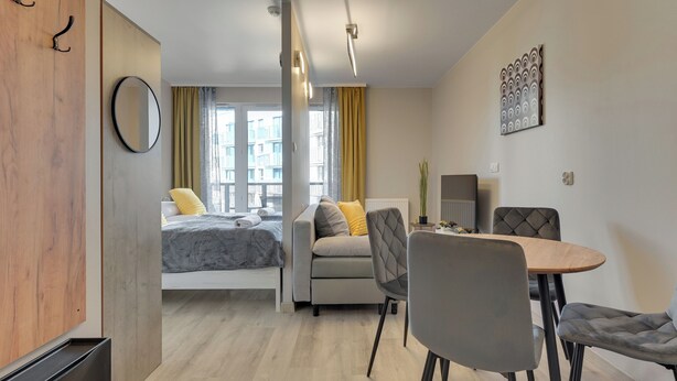 A modern room with a bed, sofa, dining table, chairs, and a mirror. - Mostek 246 - Grey by Grand Apartments (Gdańsk)