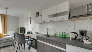 A modern kitchen with a stove, sink, and microwave, a dining area with a table and chairs, and a living area with a sofa and a plant. - Mostek 246 - Grey by Grand Apartments (Gdańsk)