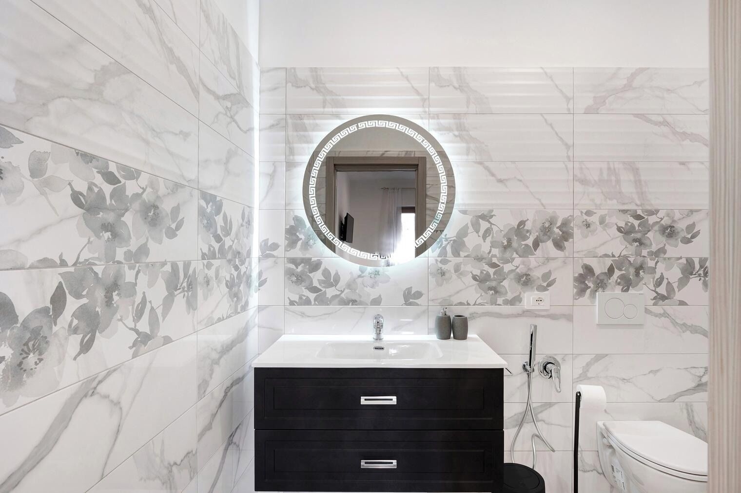 A bathroom with marble walls, a round mirror, a sink, a dark cabinet, and a toilet.