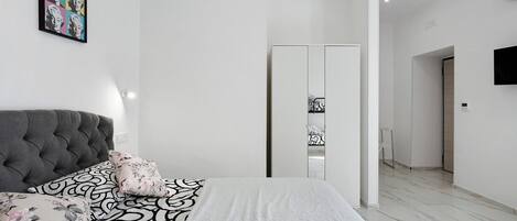 A bedroom with a tufted headboard, a bed with patterned bedding, a white closet, and a TV mounted on the wall.