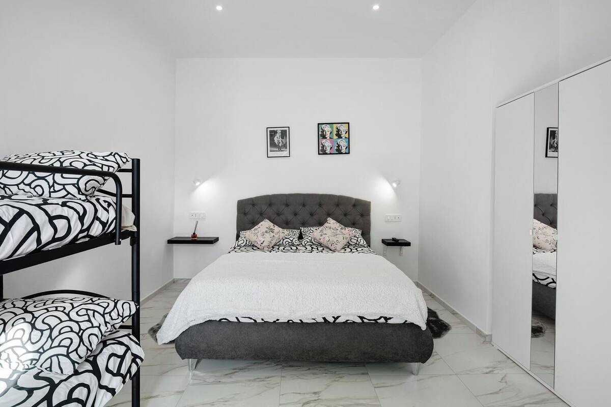 Une chambre avec un lit superposé, une tête de lit capitonnée, une table de chevet avec une lampe et deux tableaux encadrés au mur.
