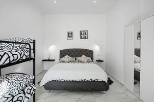 A bedroom with a bunk bed, a tufted headboard, a bedside table with a lamp, and two framed pictures on the wall.