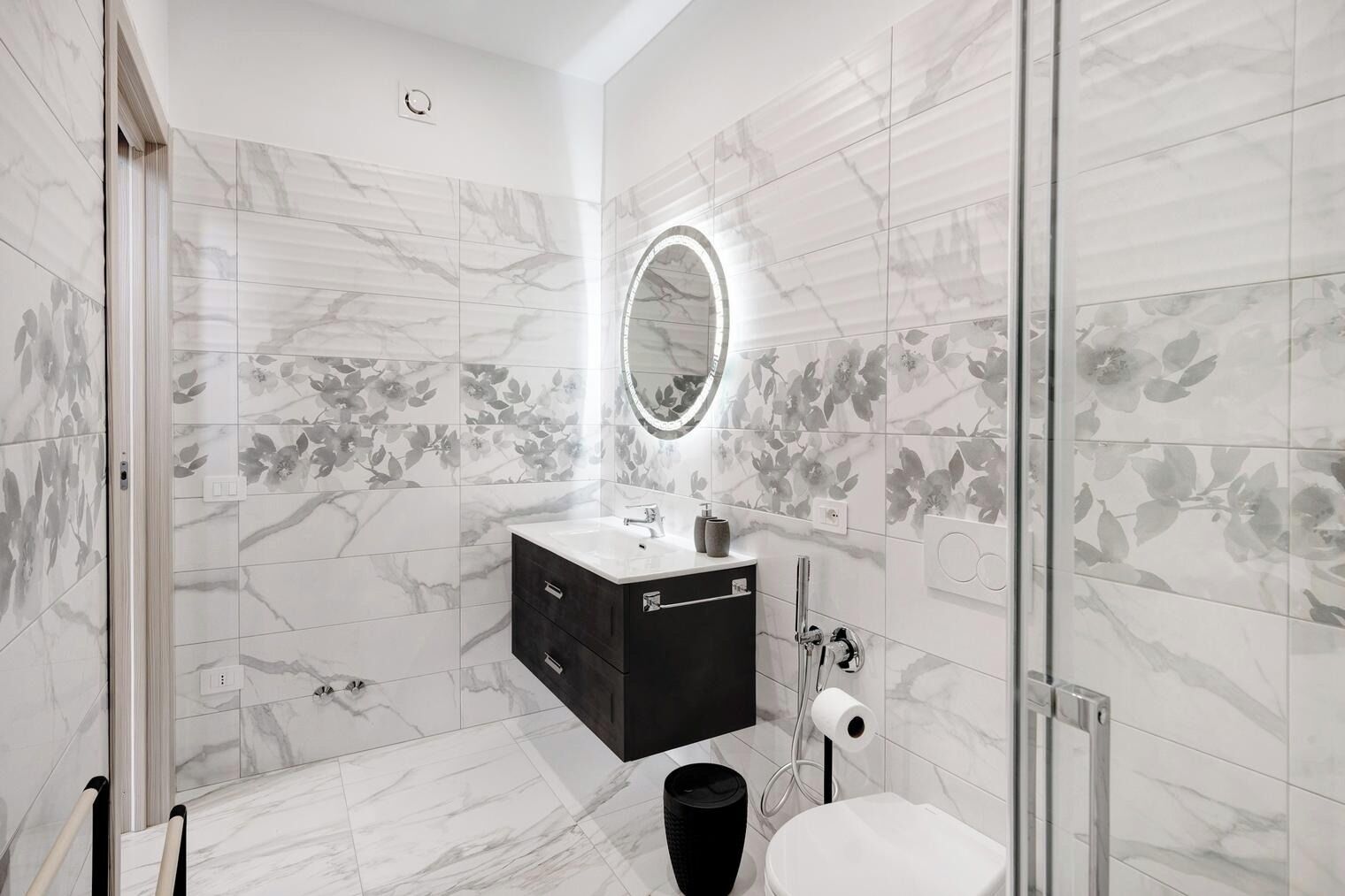 Een badkamer met een marmeren vloer, een zwart wastafelmeubel, een spiegel met een ronde lijst, en een toilet.